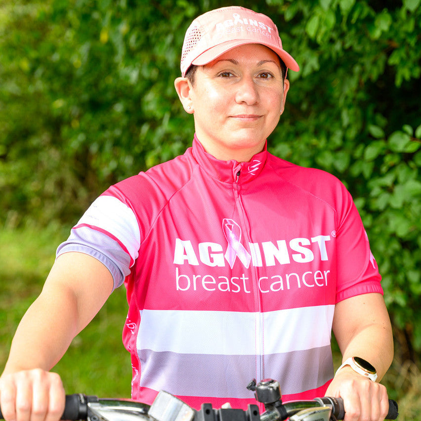 Person wearing a pink 'Against Breast Cancer' cycling outfit with a bicycle outdoors.