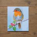 Bird with a red chest sitting on a branch with holly leaves and berries against a light blue background.