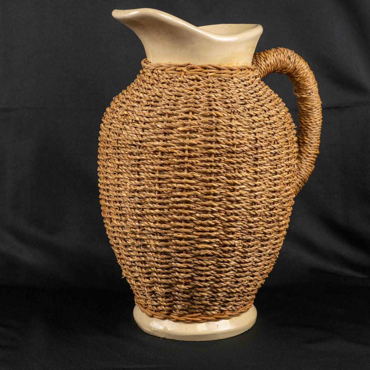 Ceramic pitcher jug beige and brown with wicker weave covering and rustic charm.