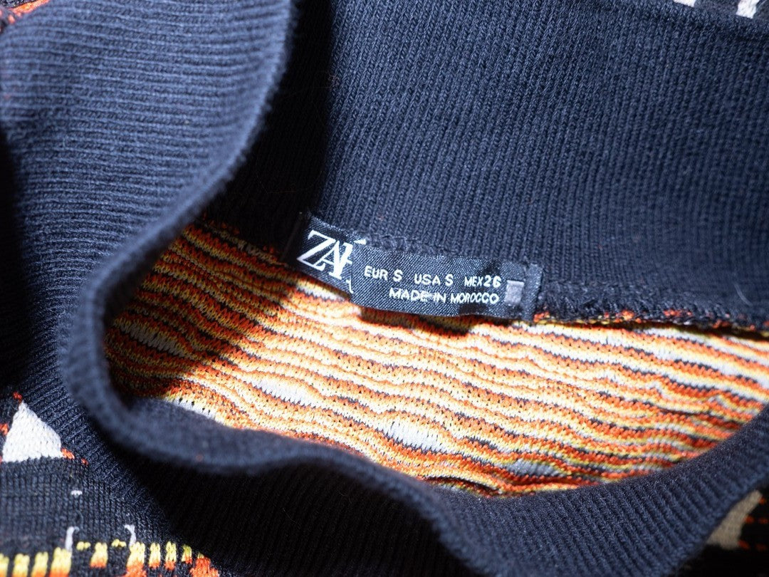 Zara black crewneck sweater with orange, yellow, and cream geometric pattern.