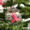 Clear Christmas ornament with a pink ribbon inside, hanging on a tree.